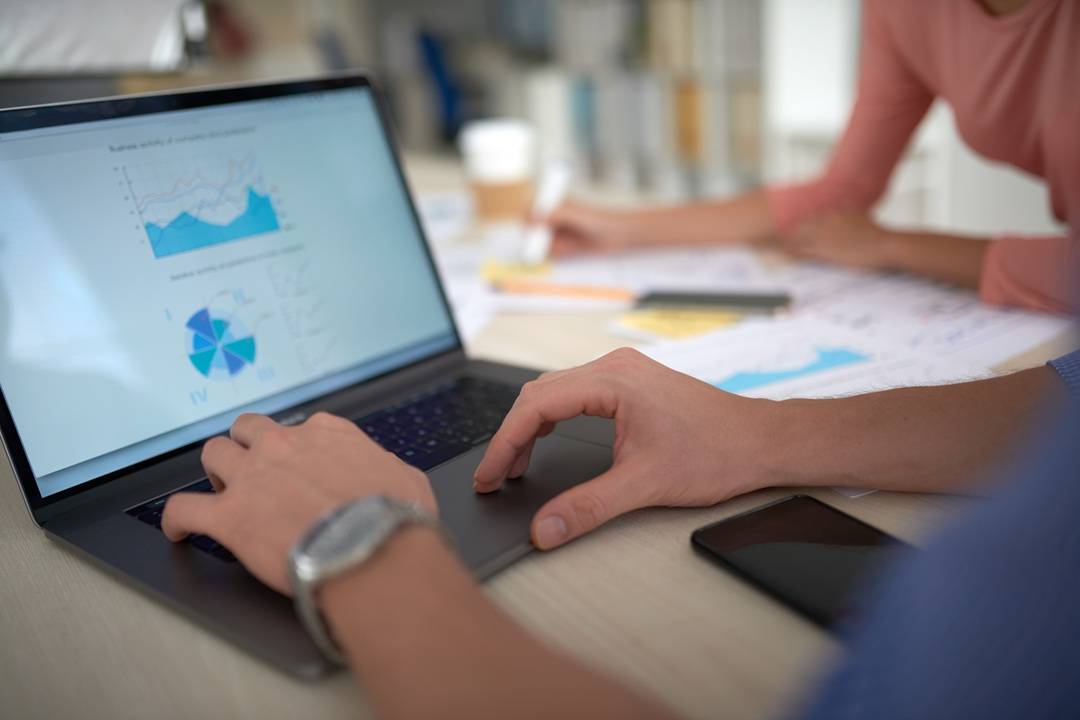 Mani al lavoro su laptop e documenti per analisi, pianificazione e controllo delle commesse.